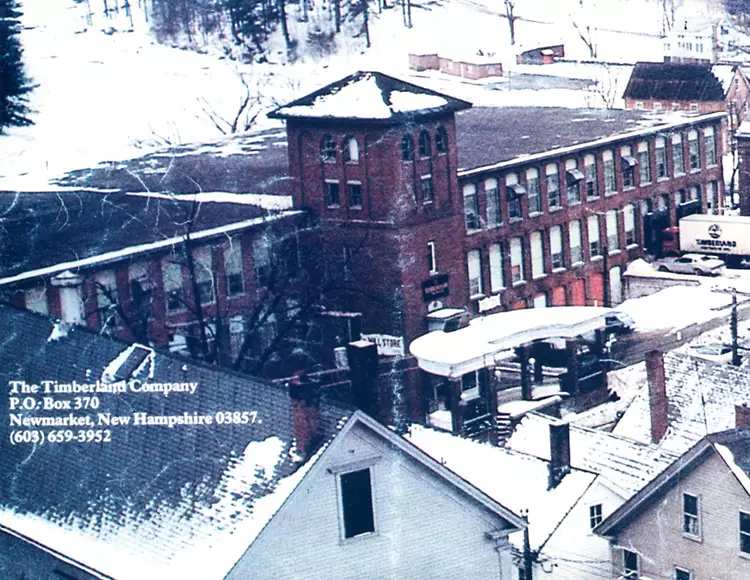 Image that's faded, of a wintertime aerial view of a brick factory with snow and a Timberland truck at a loading dock.