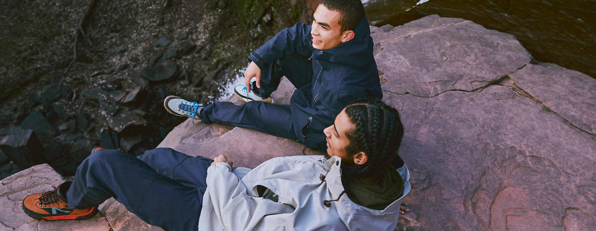 Men in Timberland clothing sitting on cliff by water
